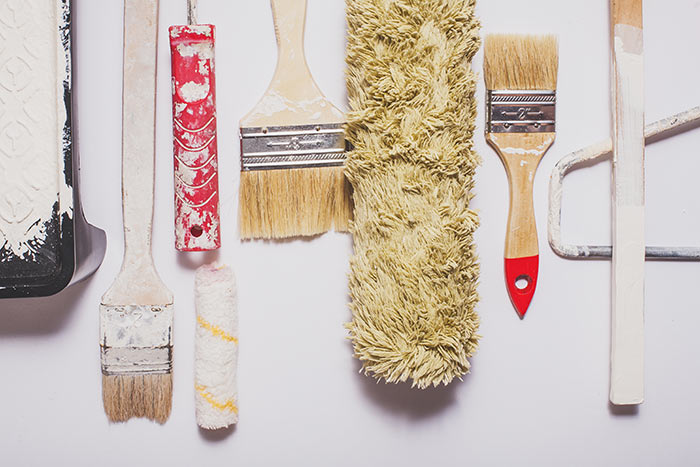 Used painting tools with red handles covered in warm white paint layed out in a composition on a plain white background