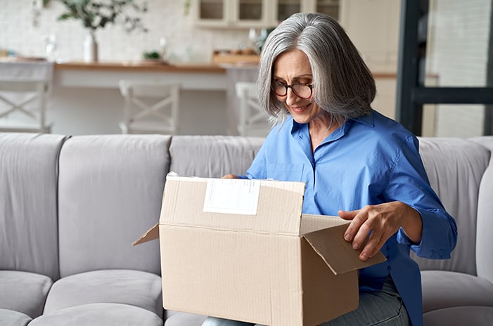 Woman sitting on a gray couch, opening a package.