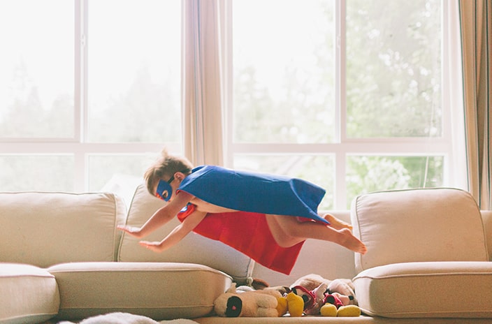 Boy with superhero cape flying over stuffed animals