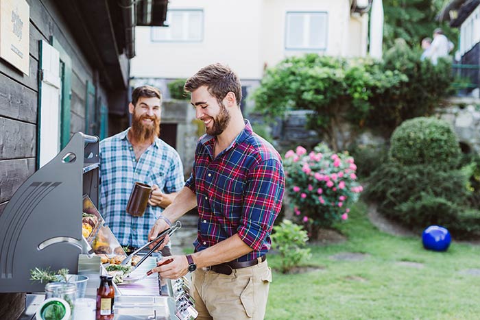 Two men cooking outdoors at barbecue station having fun