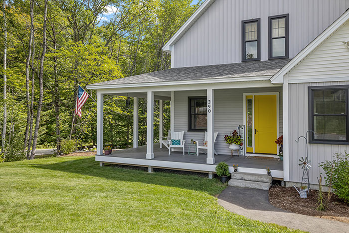 Beautiful gray porch of a modern custom new England colonial home with a garden