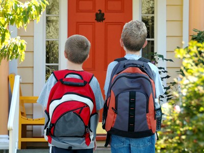 two boys with backpacks in front of home